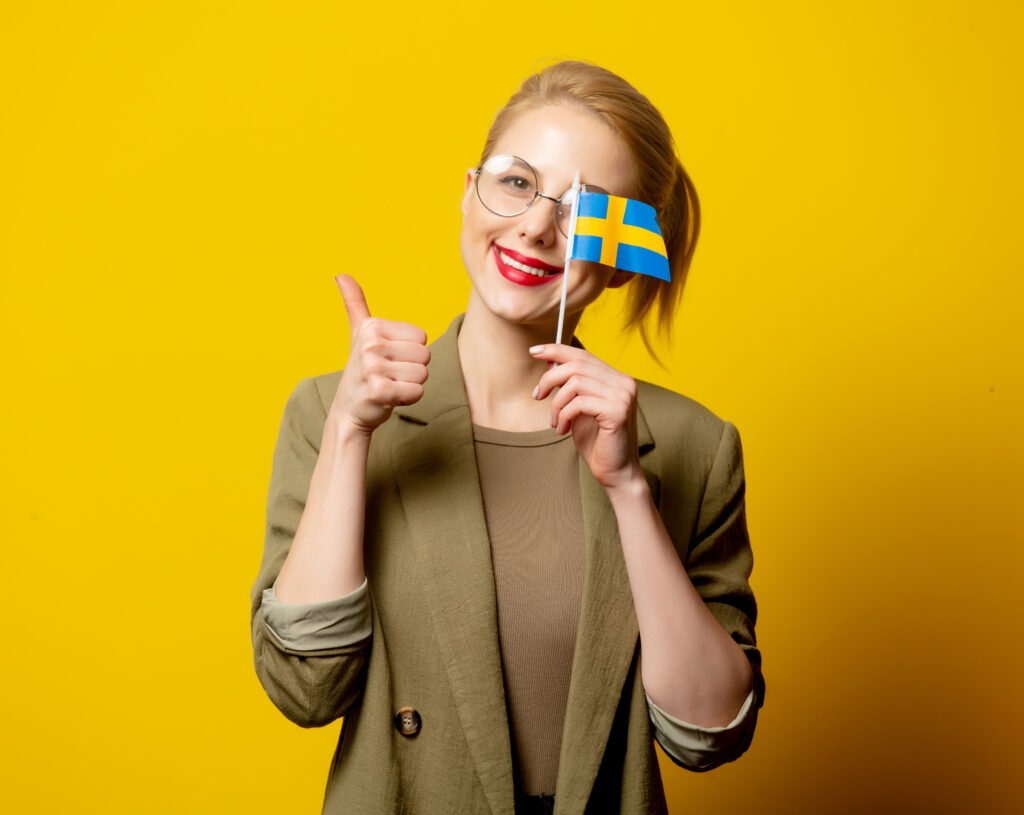 Style blonde woman in jacket with Swedish flag on yellow backgro