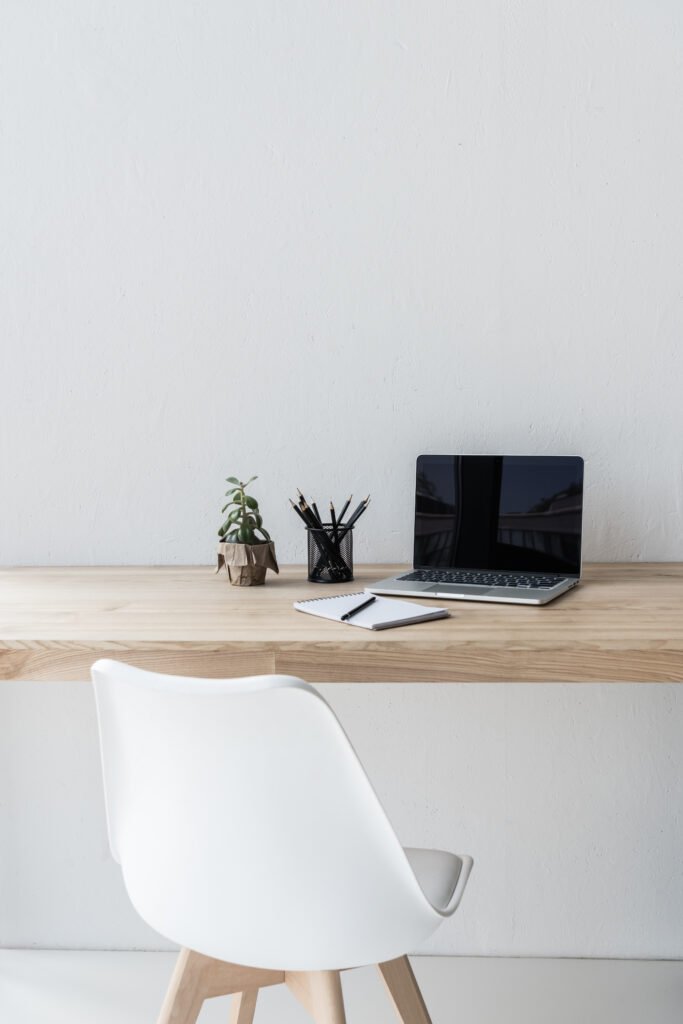 Scandinavian Workspace with Laptop and Notepad Minimal Scandinavian desk setup with laptop, notepad, pencils, and small plant on a wooden table against a white wall